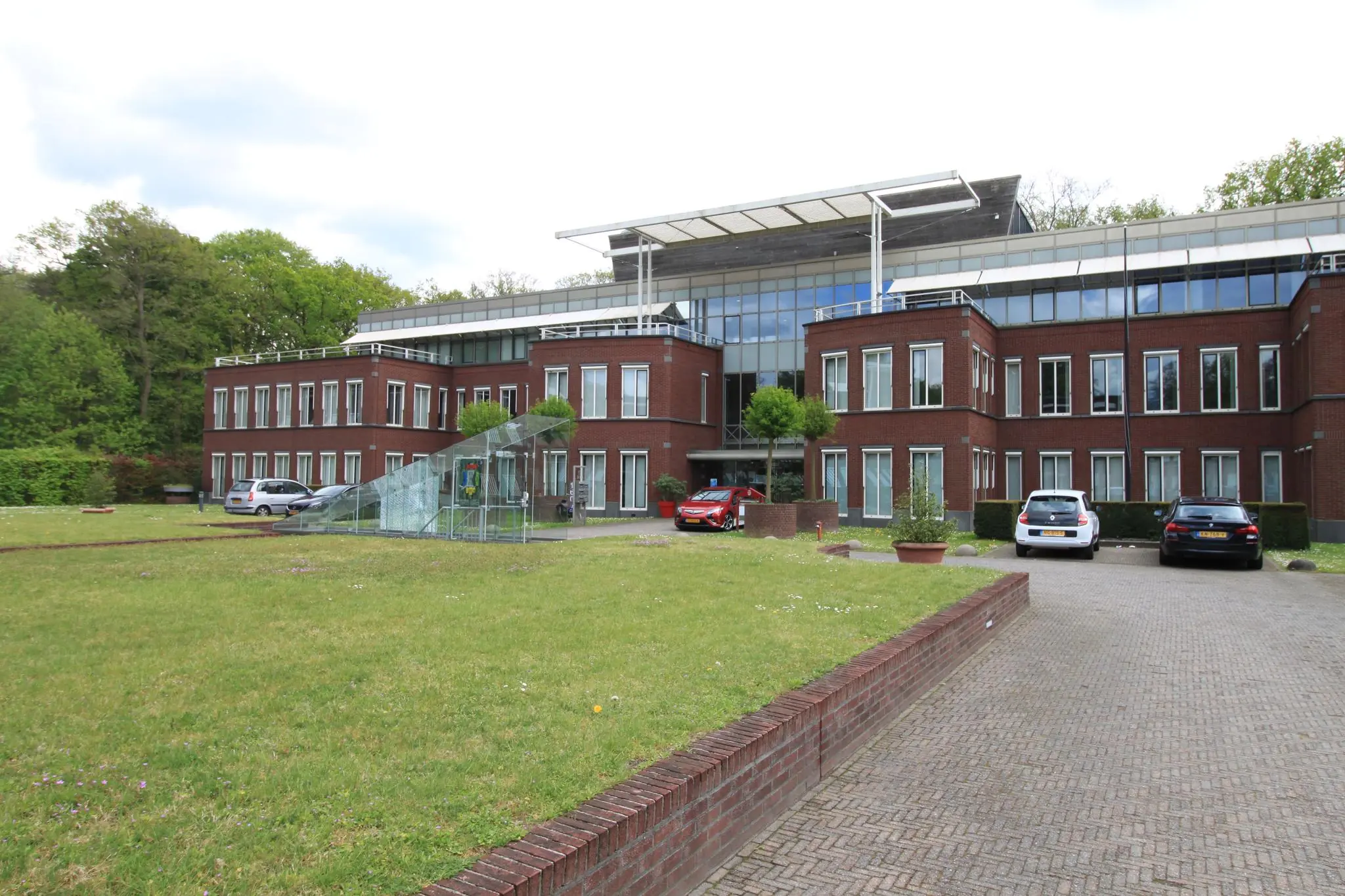 Modern kantoorgebouw aan de Arnhemse Bovenweg met een glazen entree en geparkeerde auto's op de oprijlaan.